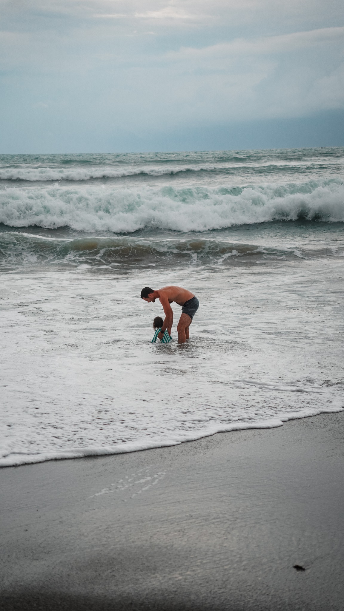 Adult helping a child in shallow ocean waves